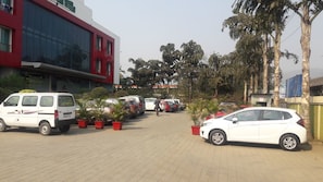 Un estacionamiento con varios coches y una camioneta blanca. Hay plantas en macetas a lo largo del pasillo.
