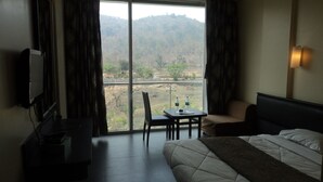 A hotel room with a bed, a desk with two water bottles, a chair, and a TV on a stand. - Royal Hills Vasai - Thane (Vasai)
