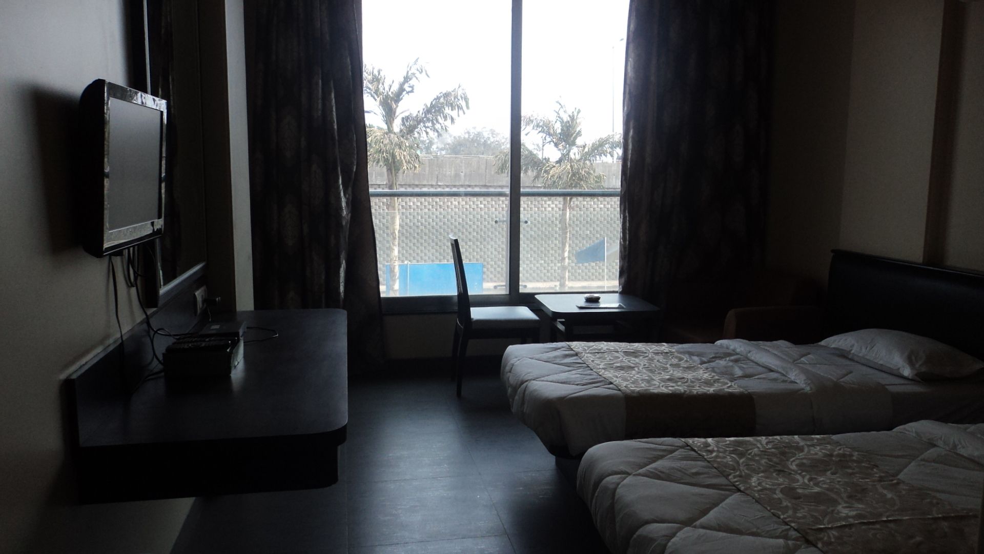 A hotel room with two beds, a desk, a chair, and a TV on the wall.