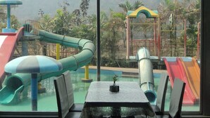 A dining area with a table and chairs, large windows with a view of a playground and hills. - Royal Hills Vasai - Thane (Vasai)