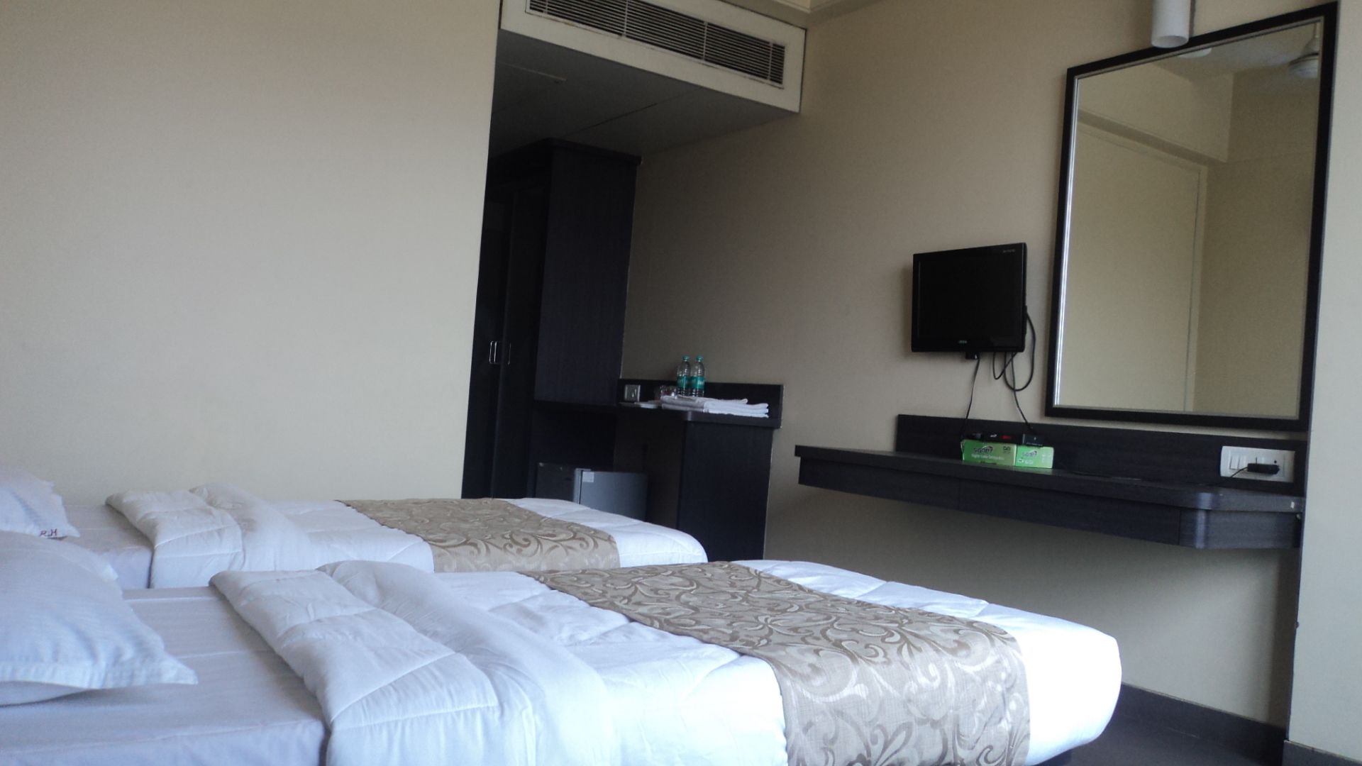 A hotel room with two beds, a desk with a mirror, and a TV.