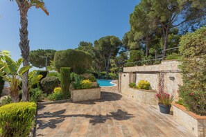 A stone pathway leading to a pool surrounded by lush greenery and trees. - Marivent Apartments by Brava Hoteles (Calonge)
