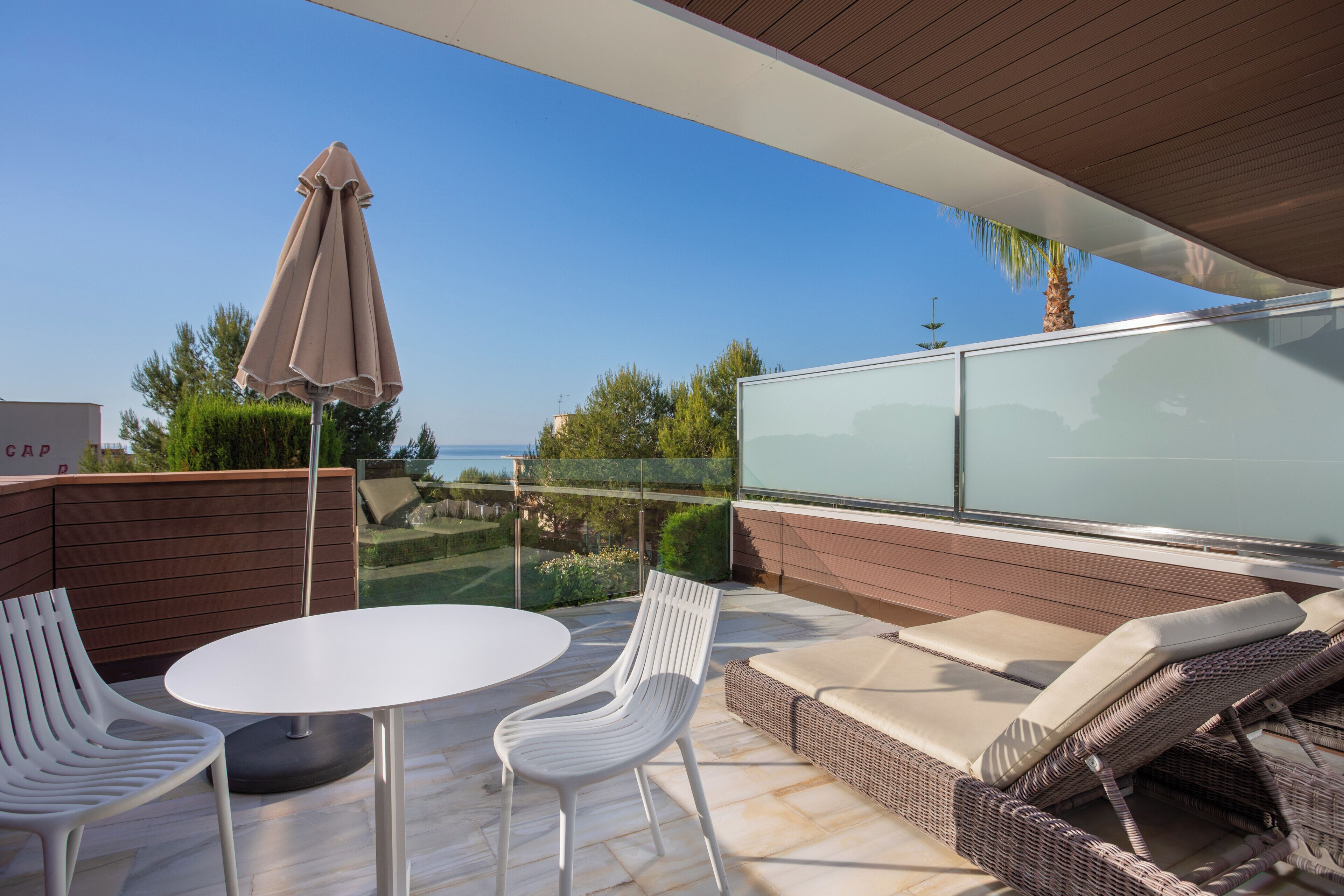 A patio with a white table, two white chairs, a wicker sofa with cushions, and a glass cabinet.