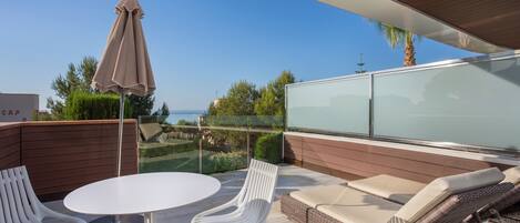 A patio with a white table, two white chairs, a wicker sofa with cushions, and a glass cabinet.