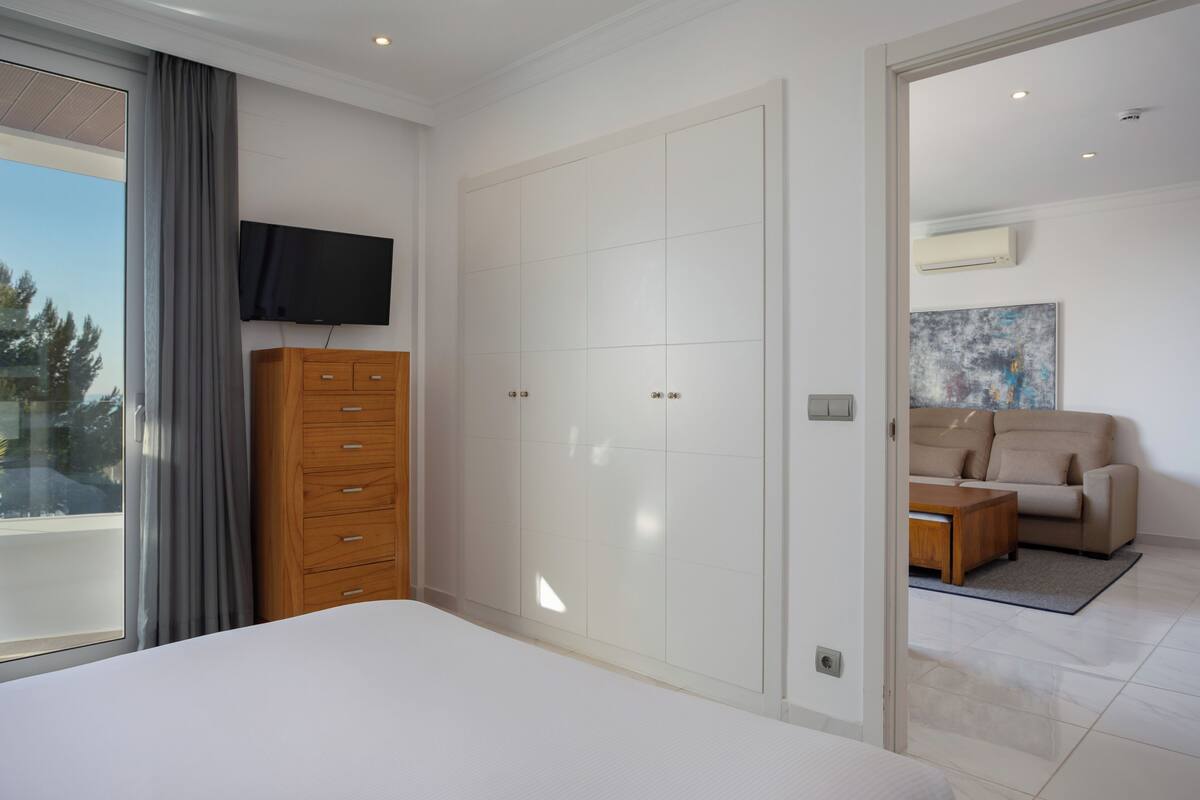 A bedroom with a bed, a wooden dresser, a TV, a wardrobe, a sofa, and a coffee table.