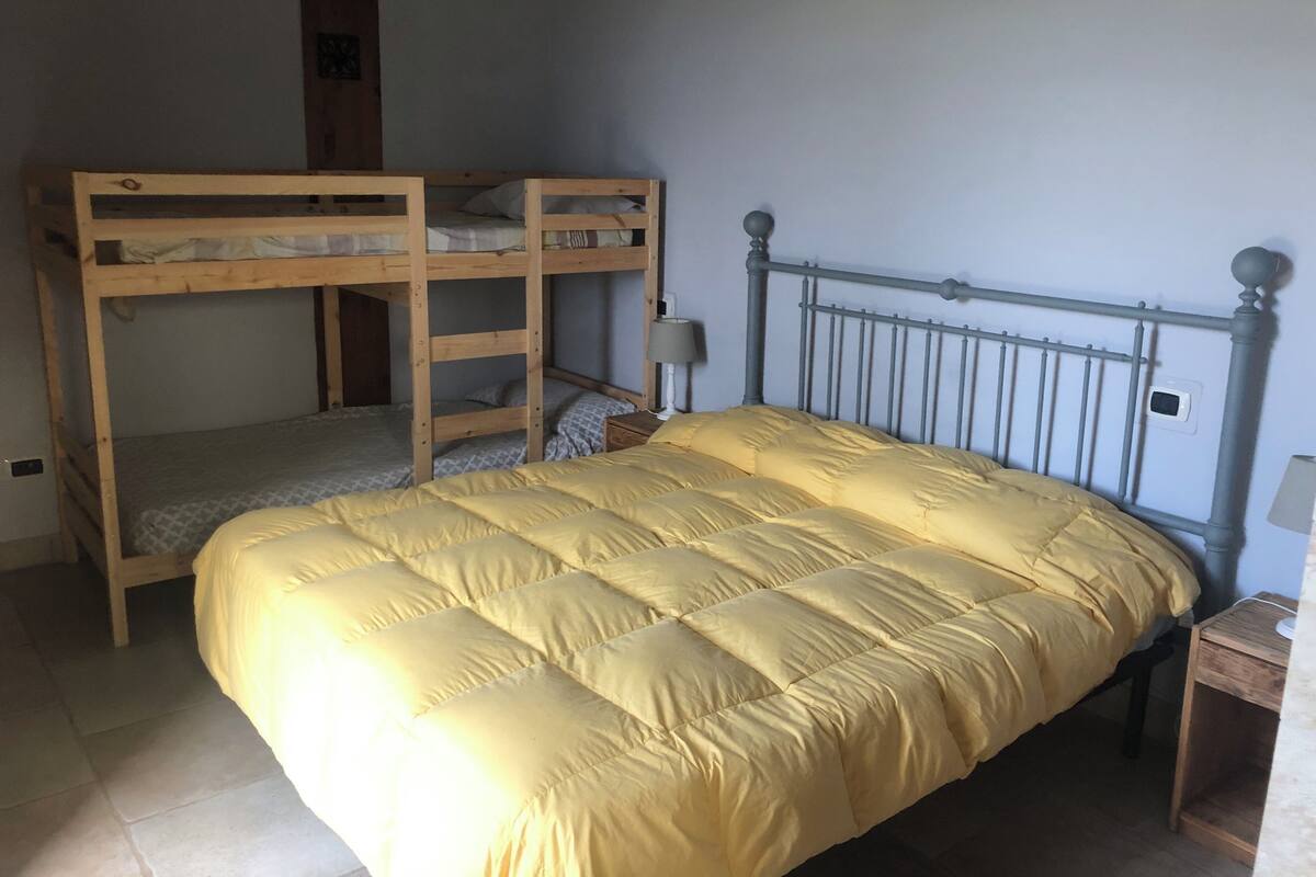 A bunk bed with a yellow quilt, a bedside table with a lamp, and a wall-mounted thermostat.