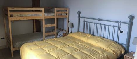 A bunk bed with a yellow quilt, a bedside table with a lamp, and a wall-mounted thermostat.
