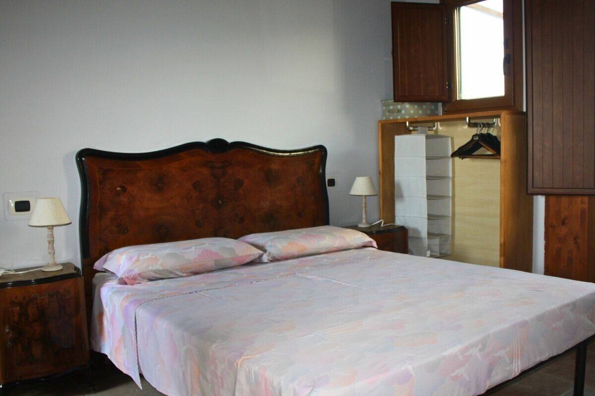 A bedroom with a wooden headboard bed, two bedside tables with lamps, a wardrobe, and a mirror.