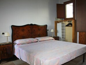 Une chambre à coucher avec un lit doté d’une tête de lit en bois, deux tables de chevet avec des lampes, une armoire et un miroir.