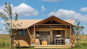 A wooden cabin with a covered porch, a small table, and a chair. - RCN Camping La ferme du Latois (Coëx)