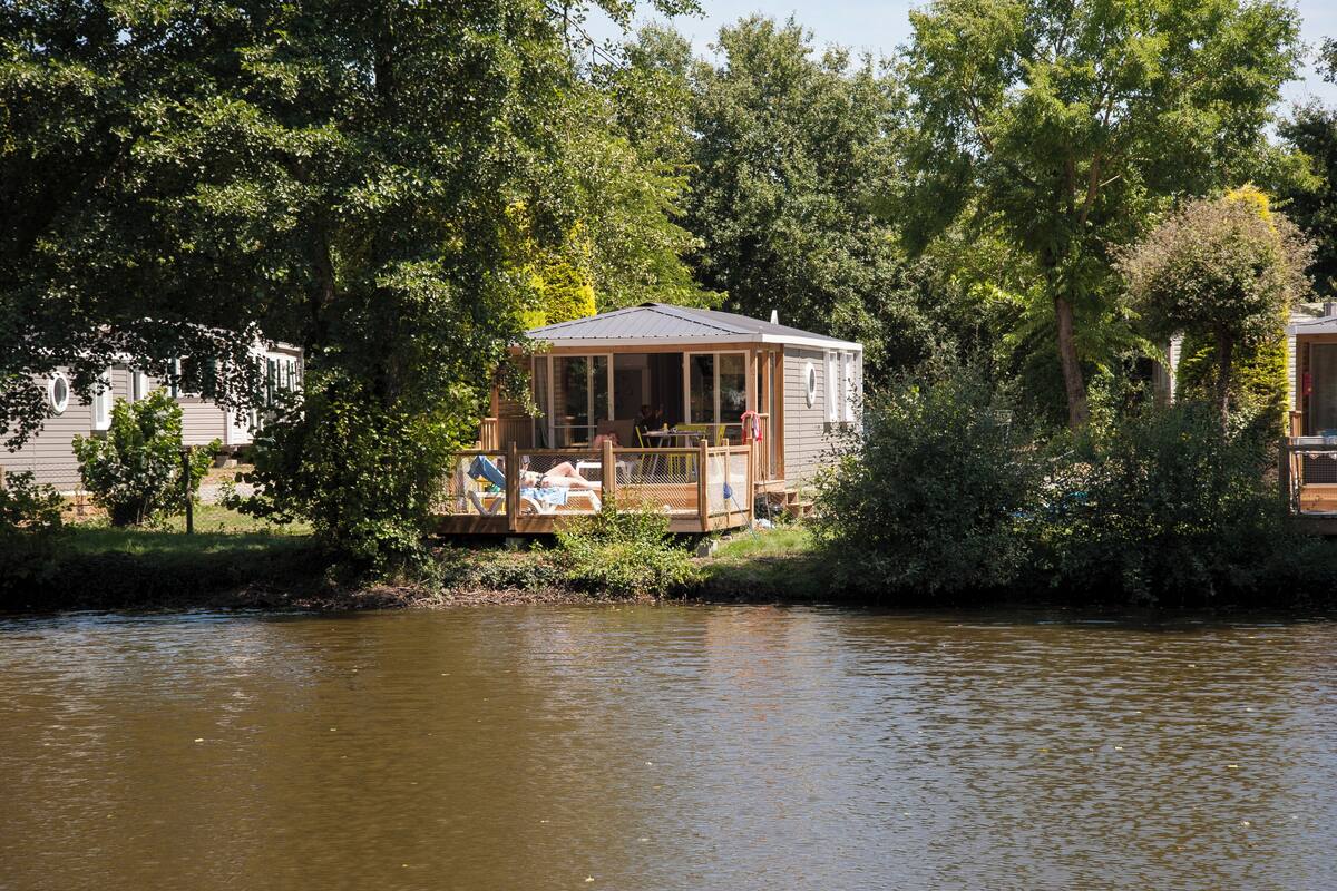 Eine Holzhütte mit Veranda, die auf einen Fluss mit Blick auf Bäume blickt.