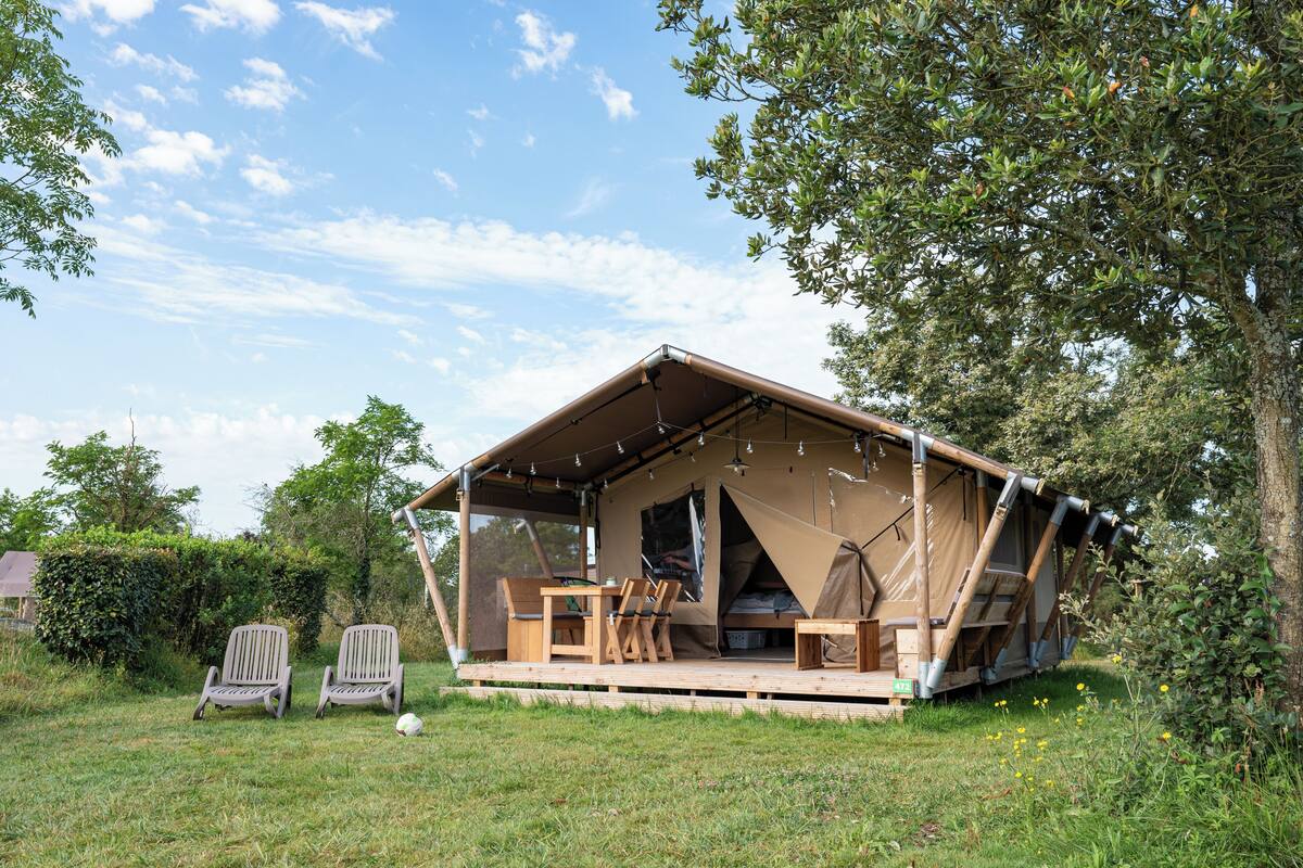 Eine Zelthütte mit Holzterrasse, Sitzgelegenheit und Kamin.