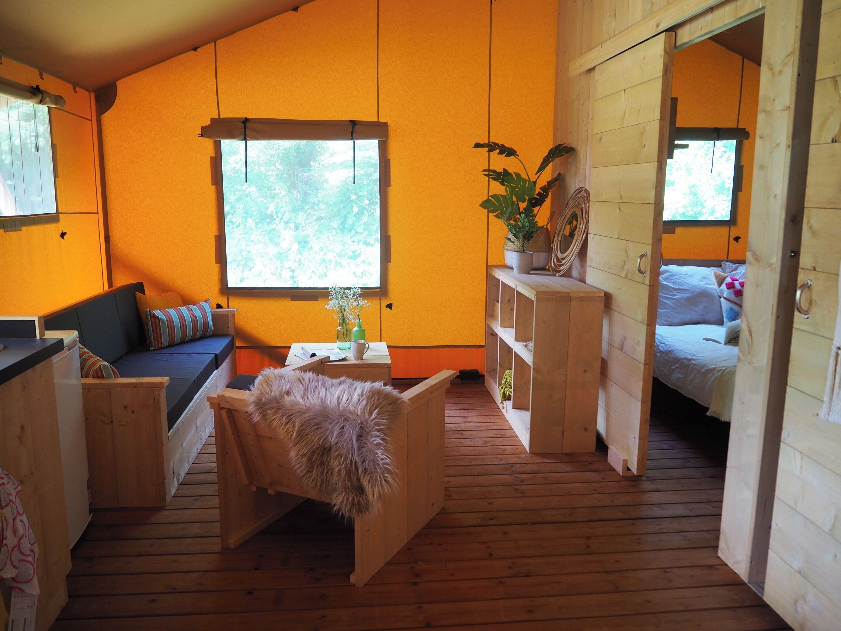 A cozy room with a wooden floor, a sofa, a small table with a plant, and a bed with pillows.