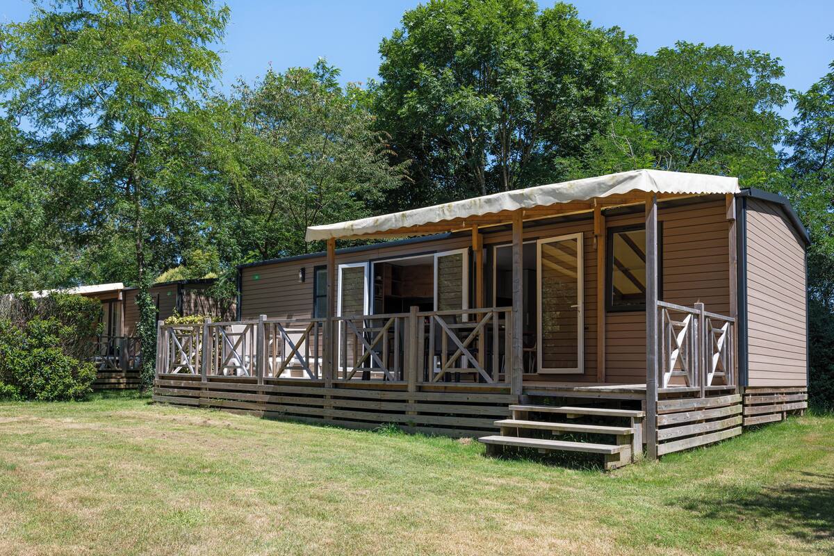 Eine Holzhütte mit überdachter Veranda und einer kleinen Terrasse, umgeben von Bäumen.