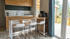 A modern kitchen with wooden cabinets, a marble backsplash, a gas stove, and a bar area with stools. - RCN Camping La ferme du Latois (Coëx)