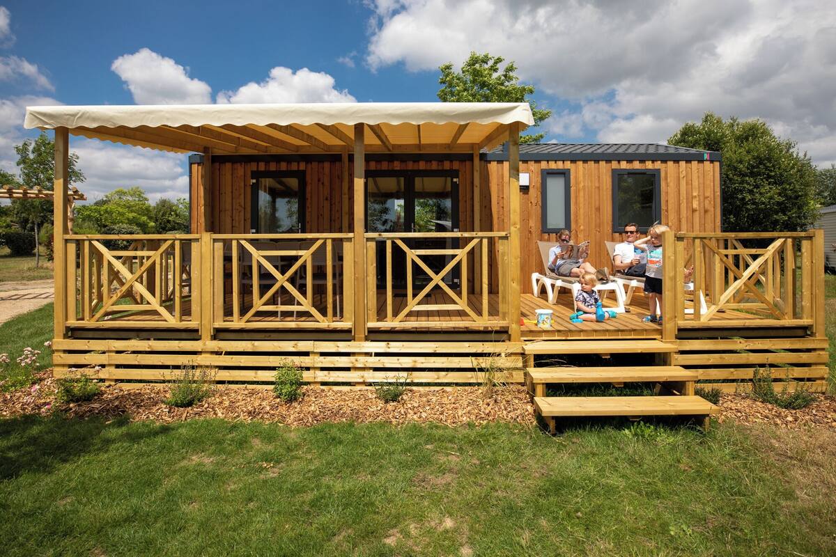 Eine Holzhütte mit überdachter Veranda, Sitzgelegenheiten im Freien und einem kleinen Tisch.