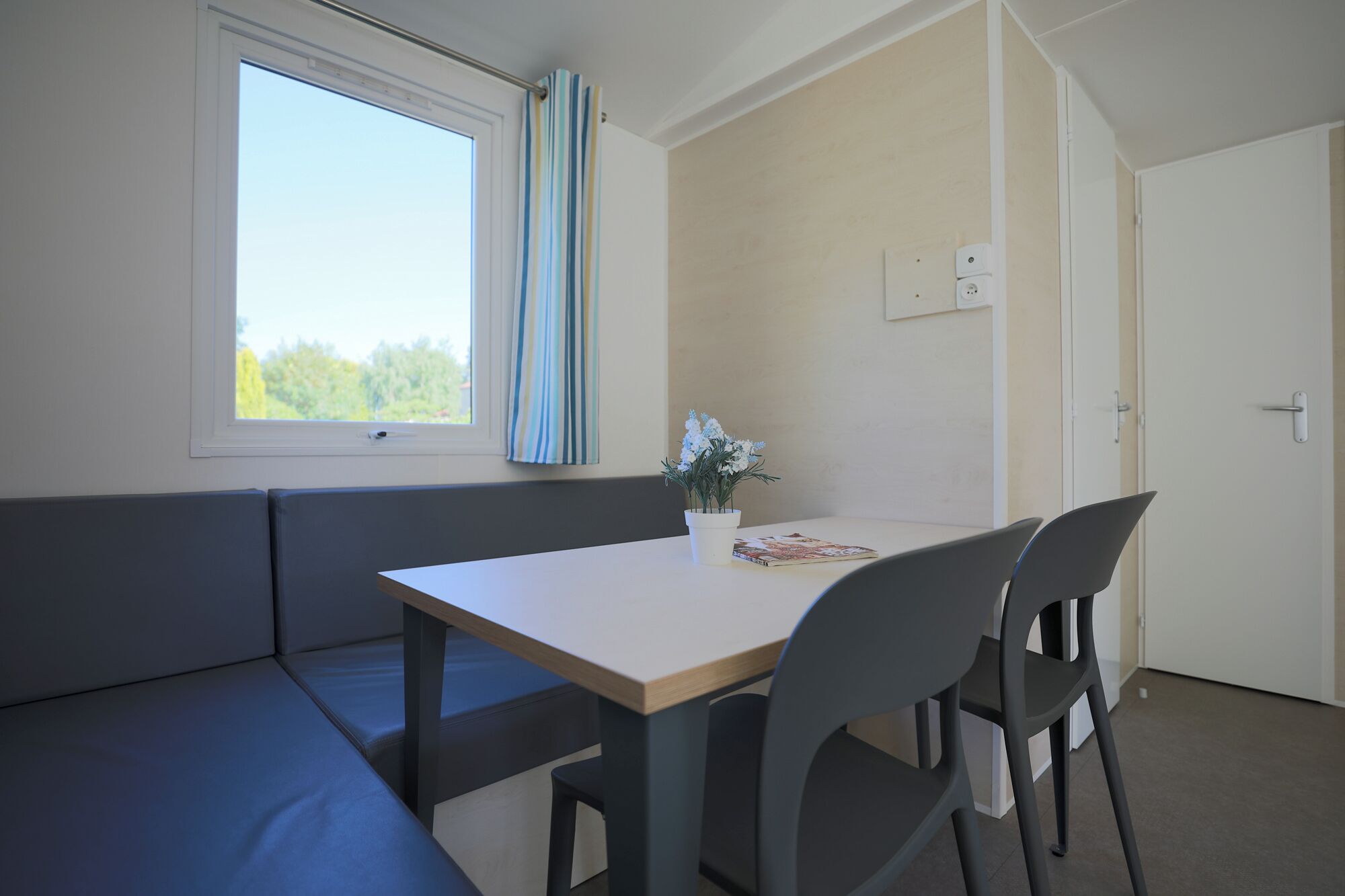 A room with a window, a table, two chairs, a bench, and a potted plant.