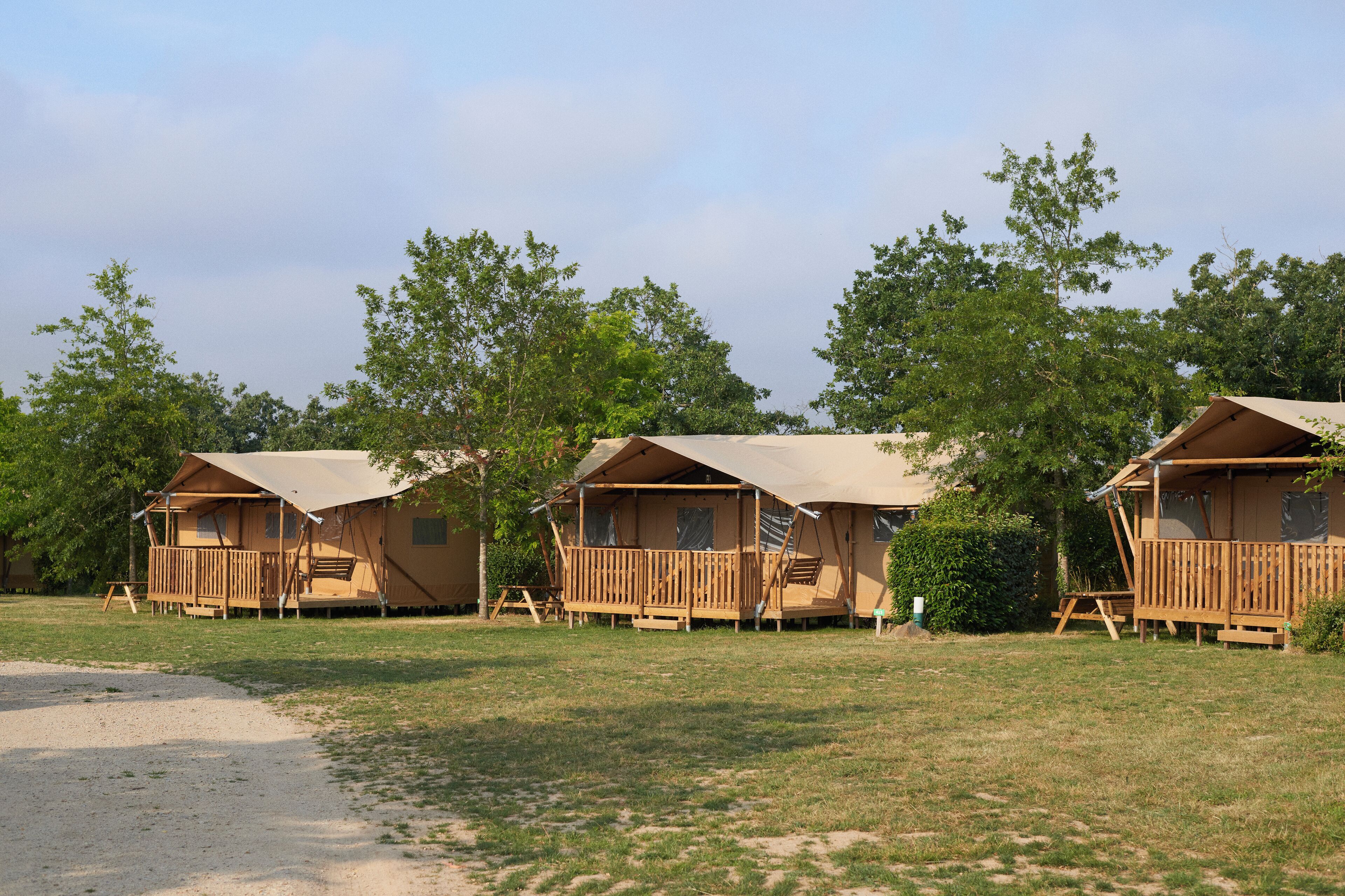 A row of wooden cabins with a covered deck, surrounded by trees.