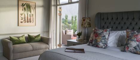 A bedroom with a bed, a sofa, a window with curtains, and a wall-mounted picture.