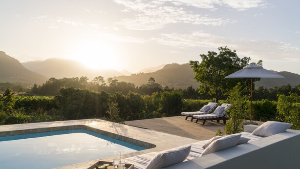 Un espace aménagé au bord de la piscine, avec une terrasse en bois, des chaises longues et une table où sont servis des boissons et des en-cas.