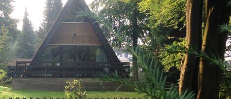 A triangular wooden structure surrounded by trees and a fence.