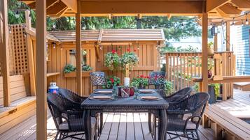 Una terraza de madera con una pérgola, mobiliario exterior y plantas en macetas.