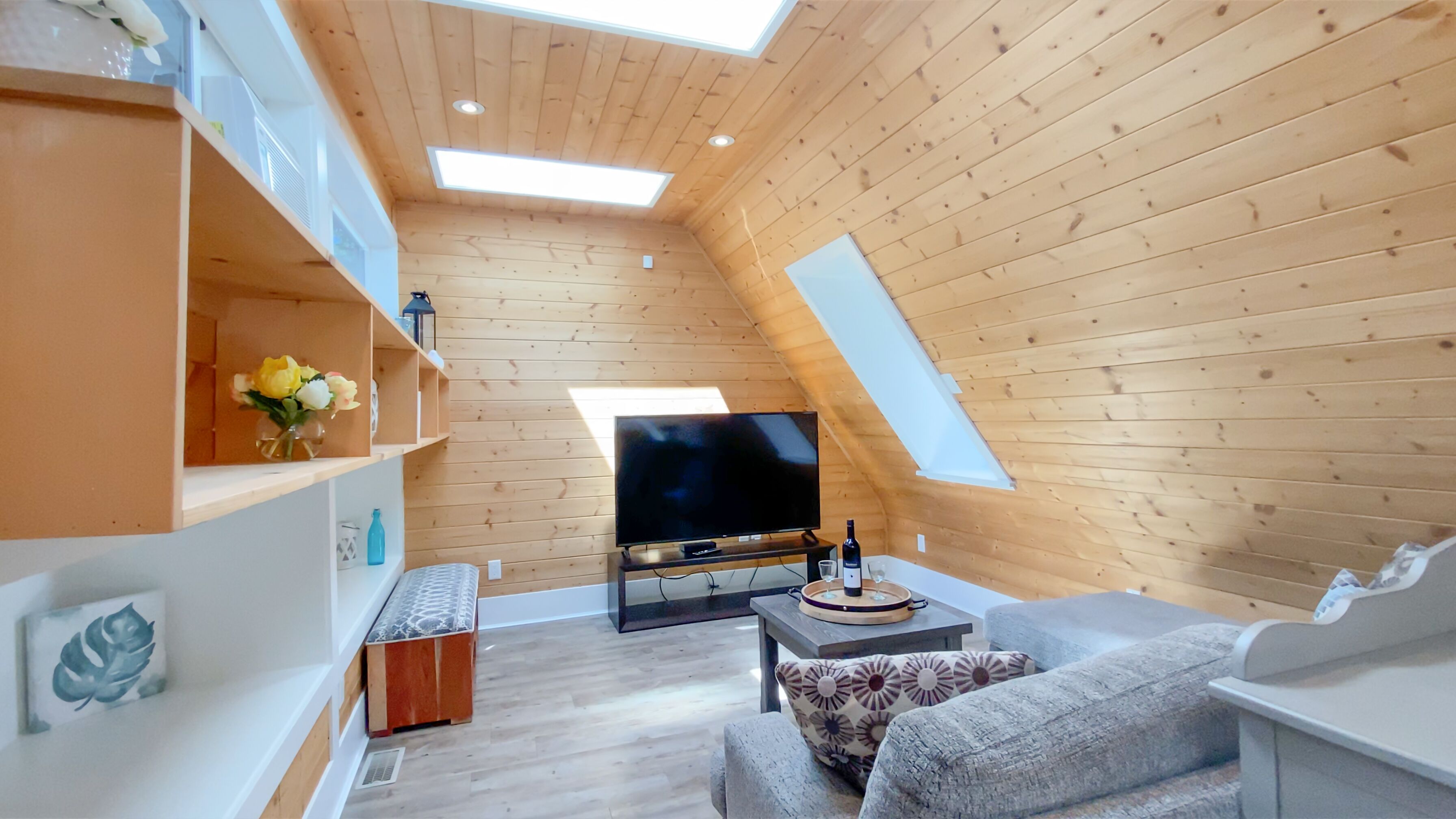 Acogedor dormitorio en ático con paredes de madera, un televisor de pantalla plana, un sofá y una pequeña mesa con una botella y un vaso.
