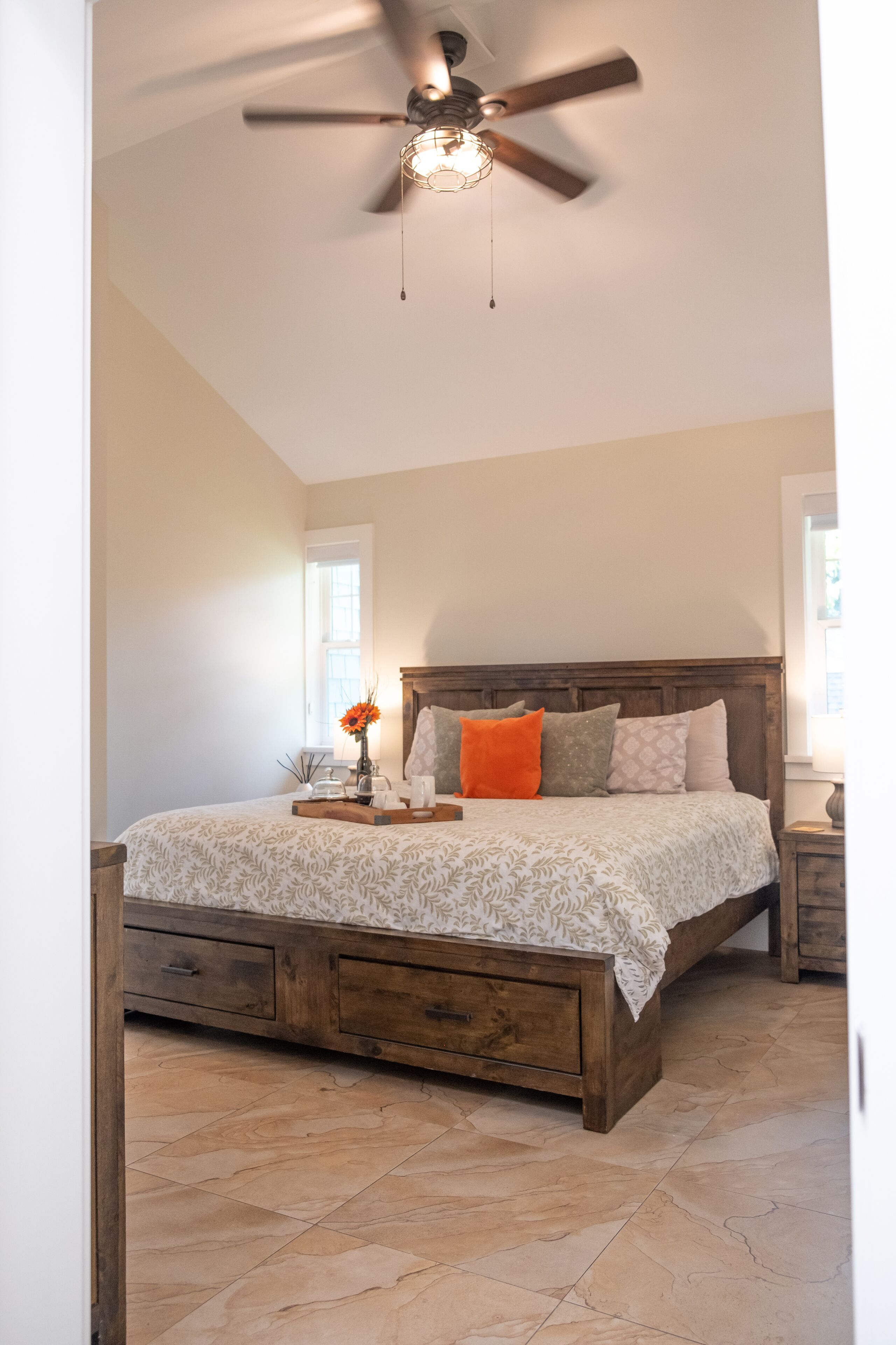 Een slaapkamer met een houten bed, een plafondventilator en een nachtkastje met een lamp.