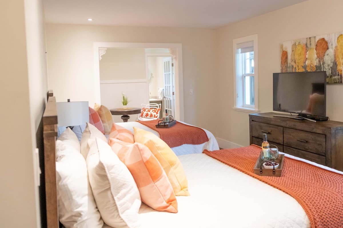 A bedroom with two beds, a TV, a dresser, and a painting on the wall.