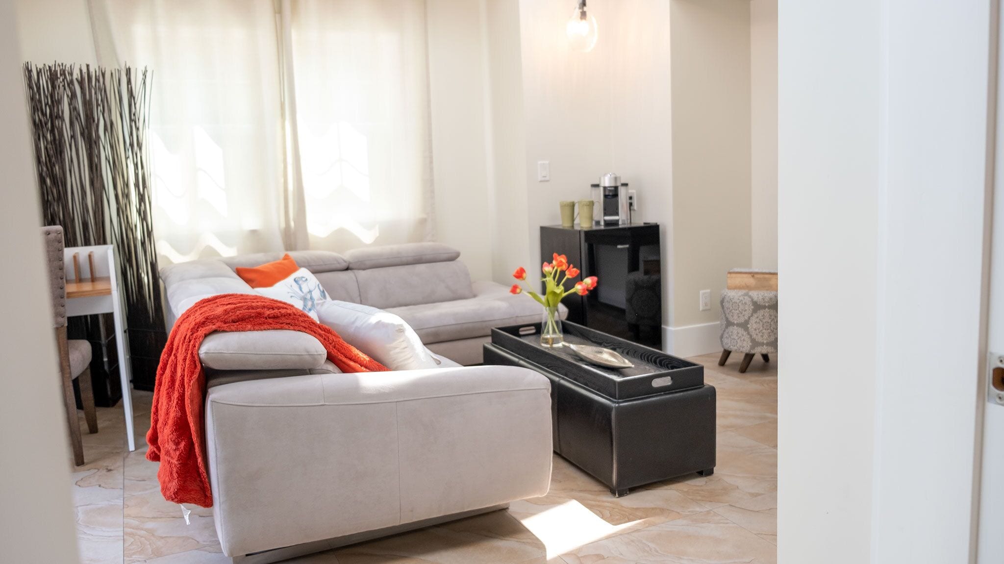 A modern living room with a grey sofa, a red throw blanket, and a vase with flowers on a black coffee table.