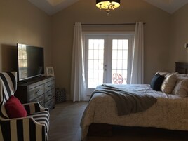 Un dormitorio con cama, televisor en una cómoda, una silla y ventana con cortinas.