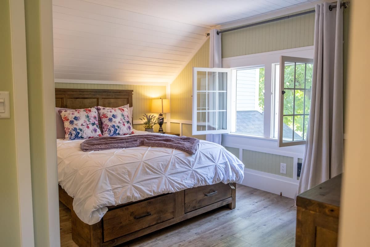 A bedroom with a large bed, wooden headboard, and a window with curtains.