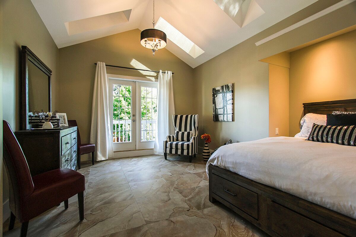 A bedroom with a large bed, a chair, a dresser, and a desk with a mirror.