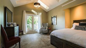 A bedroom with a large bed, a chair, a dresser, and a desk with a mirror.