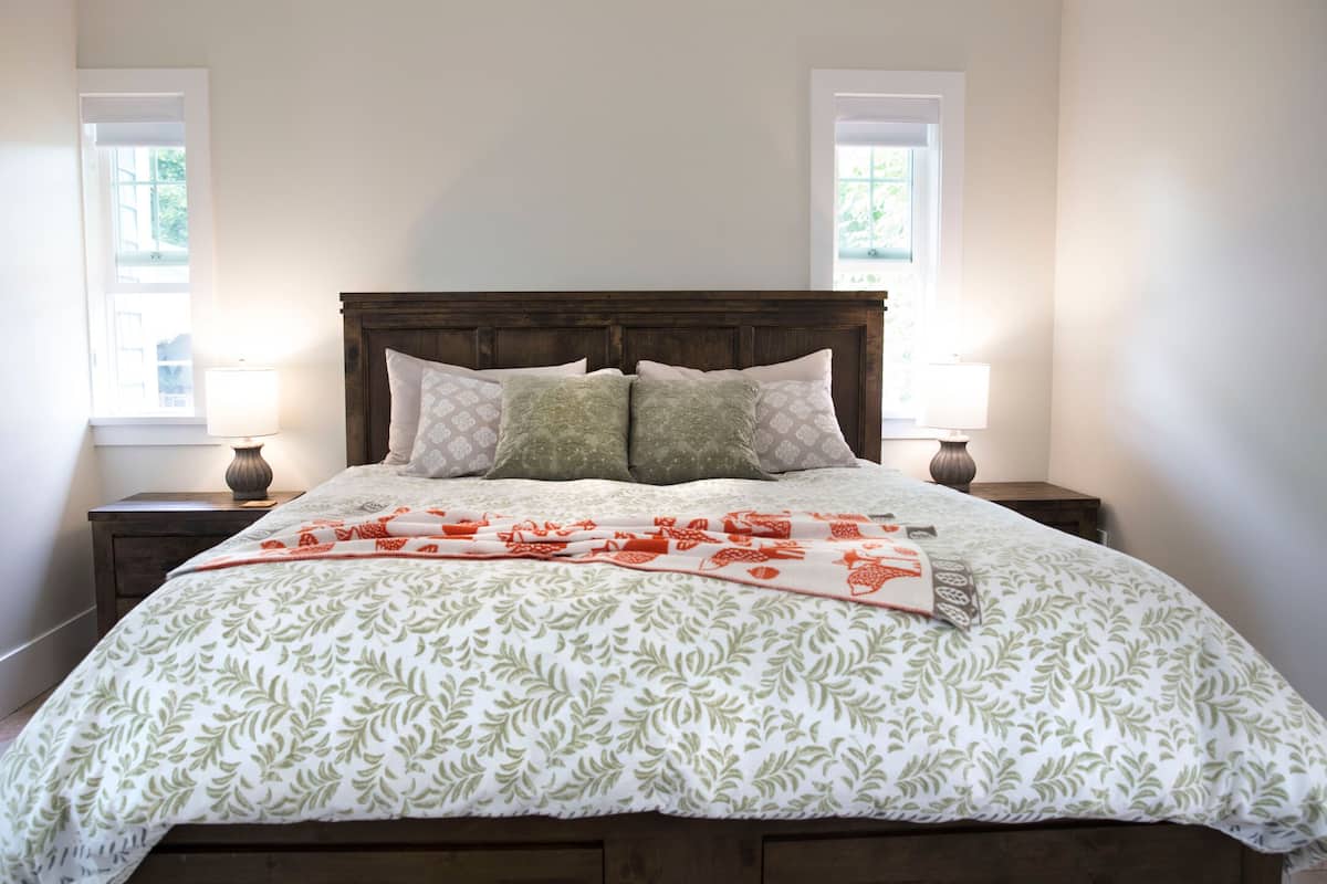 A neatly made bed with a patterned bedspread, two bedside lamps, and a window on each side.