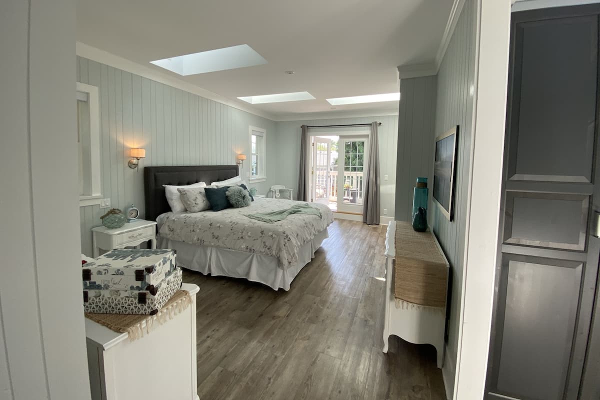 A bedroom with a bed, bedside tables, a nightstand, a window, and a door leading to a balcony.