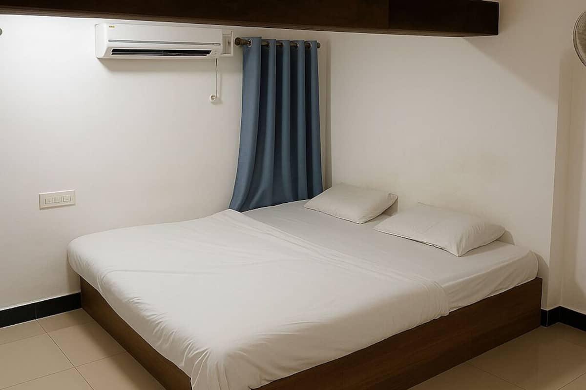 Una cama individual con cabecera de madera, cortina azul y un equipo de aire acondicionado instalado en la pared.