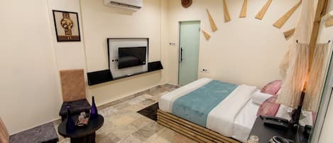 A hotel room with a bed, a TV mounted on the wall, a chair, a small table, and a tray with items.