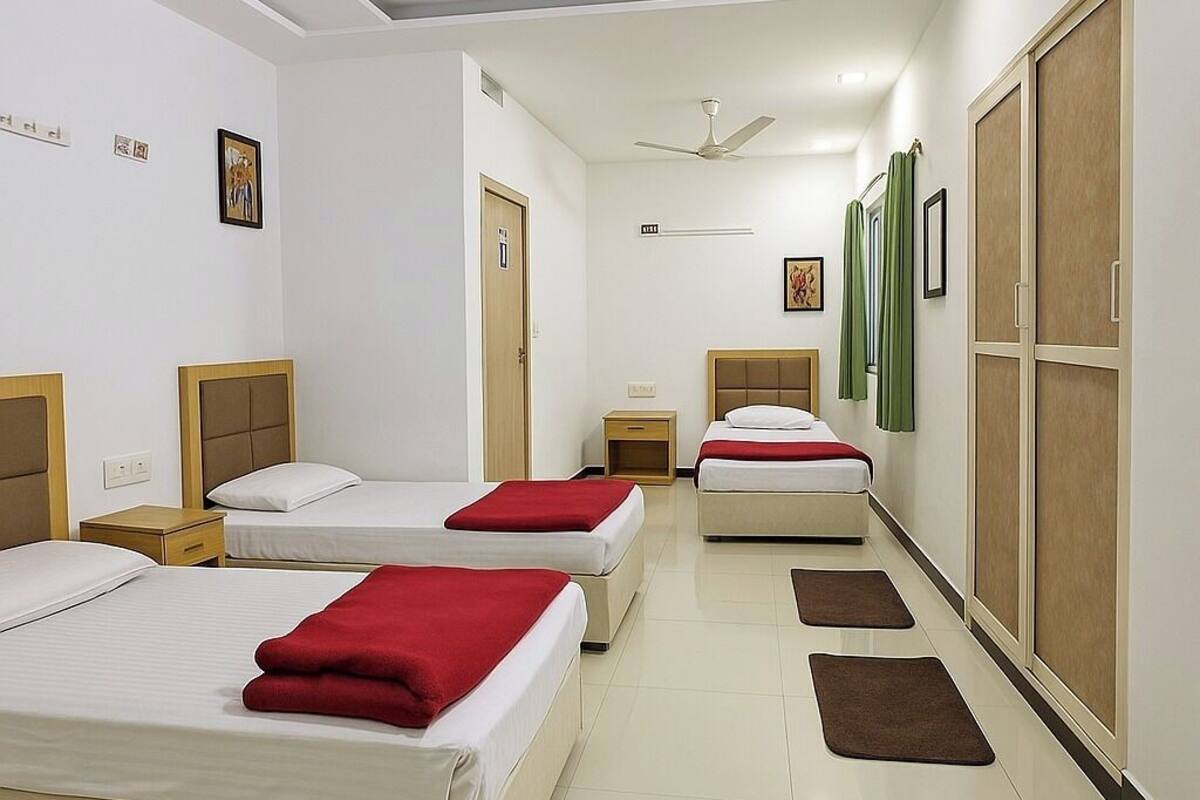 Habitación de hotel con tres camas, un ventilador de techo y un pasillo con puertas.