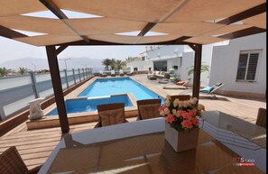 A rooftop pool area with a wooden deck, lounge chairs, and a table with a vase of flowers. - Sweethome26 LUXURY VILLA SEE VIEW (Eilat)