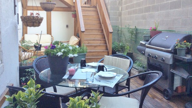 A patio with a glass table, chairs, a grill, and potted plants. - BlancNoir Bed & Breakfast (Baltimore)