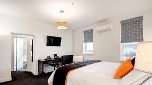 A hotel room with a large bed, a desk, a chair, a television, and a window with patterned curtains. - BlancNoir Bed & Breakfast (Baltimore)