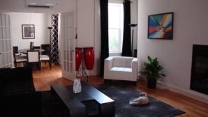 A living room with a black sofa, a white armchair, a coffee table, a potted plant, and a painting on the wall. - BlancNoir Bed & Breakfast (Baltimore)