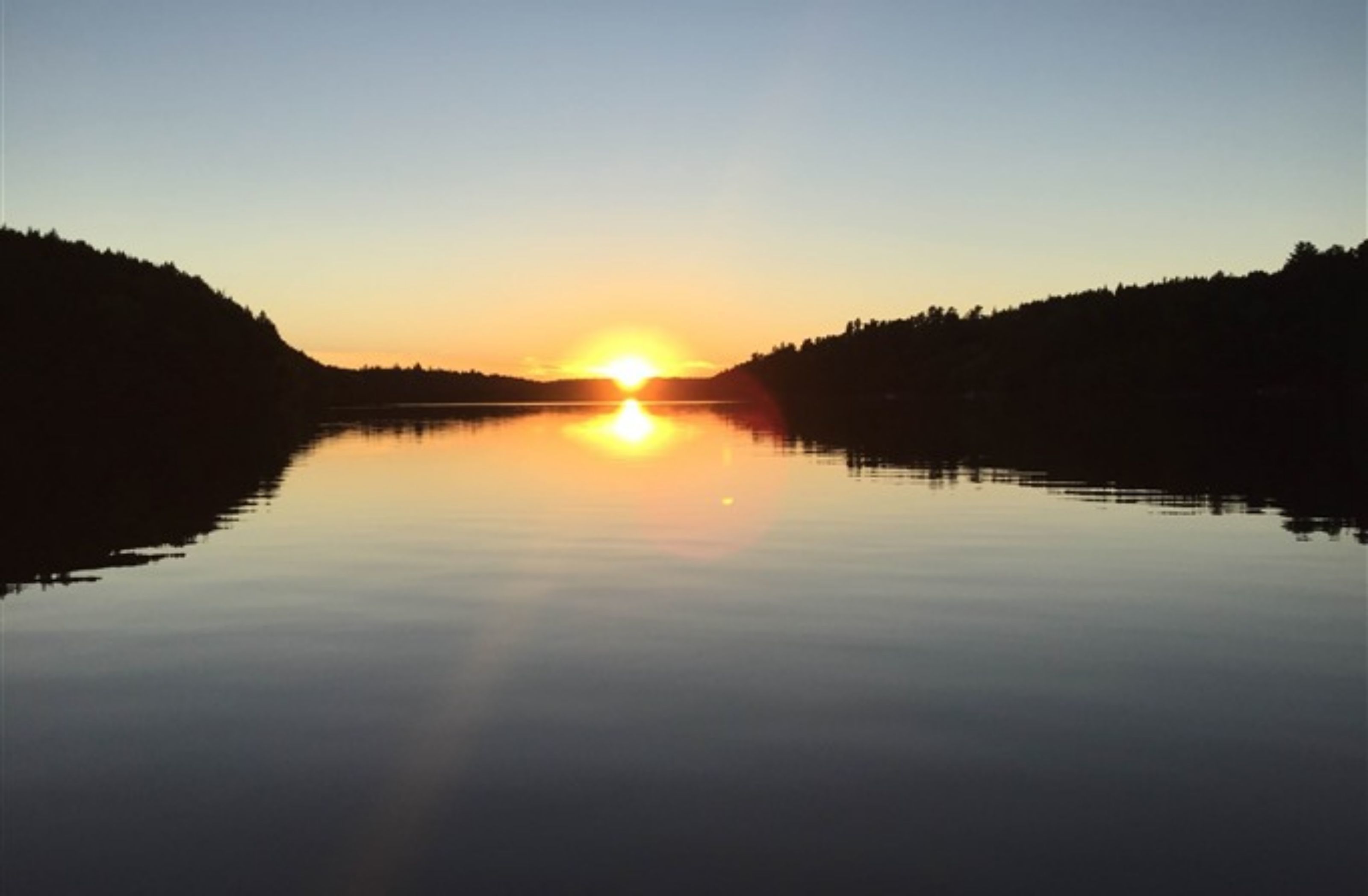 Um lago tranquilo ao pôr do sol, com céu claro.