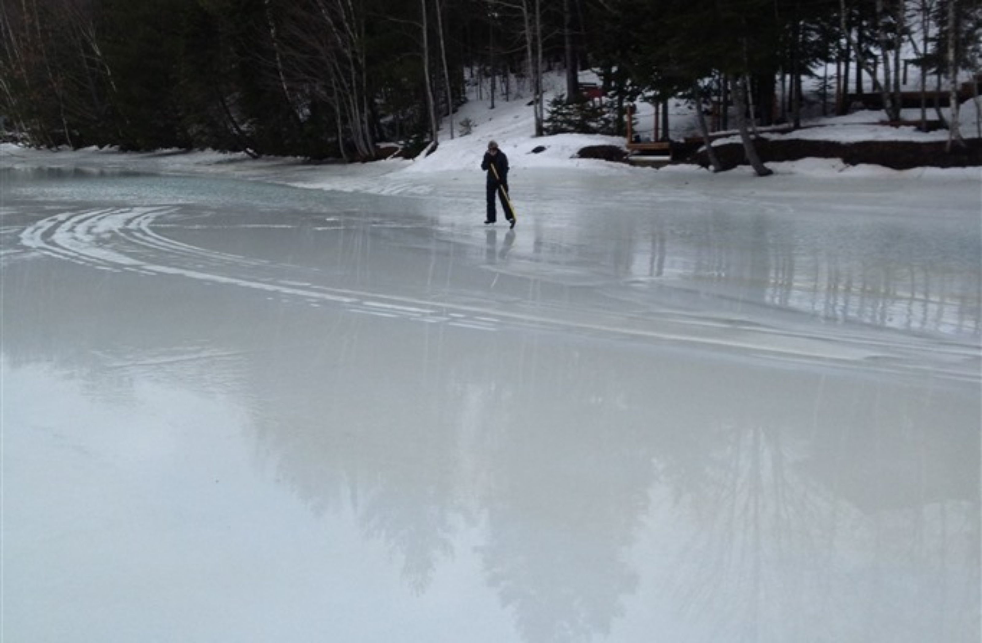 A person ice skating on a frozen lake surrounded by trees.