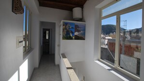 A narrow hallway with a window on the right, a door at the end, and a wall-mounted light fixture. - Loft Lipari (Lipari)