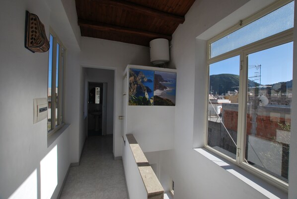 A narrow hallway with a window on the right, a door at the end, and a wall-mounted light fixture.