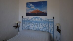 A bedroom with a bed, a decorative headboard, two wall-mounted lamps, and a framed picture of a volcano on the wall. - Loft Lipari (Lipari)
