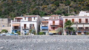 A coastal building with balconies, a rocky foreground, and a hillside in the background. - Loft Lipari (Lipari)