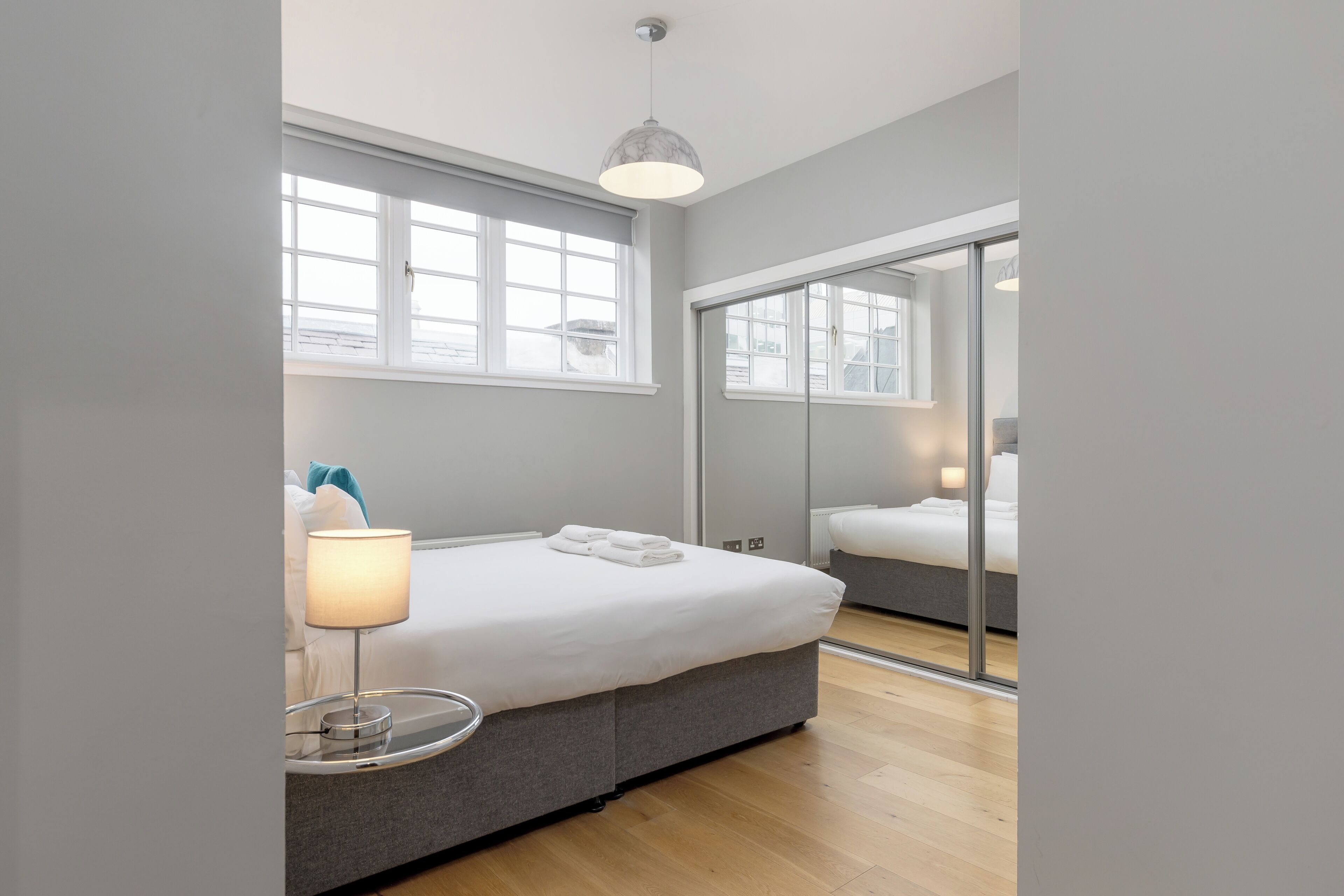 Een moderne slaapkamer met een bed, bedlamp en een grote spiegel.